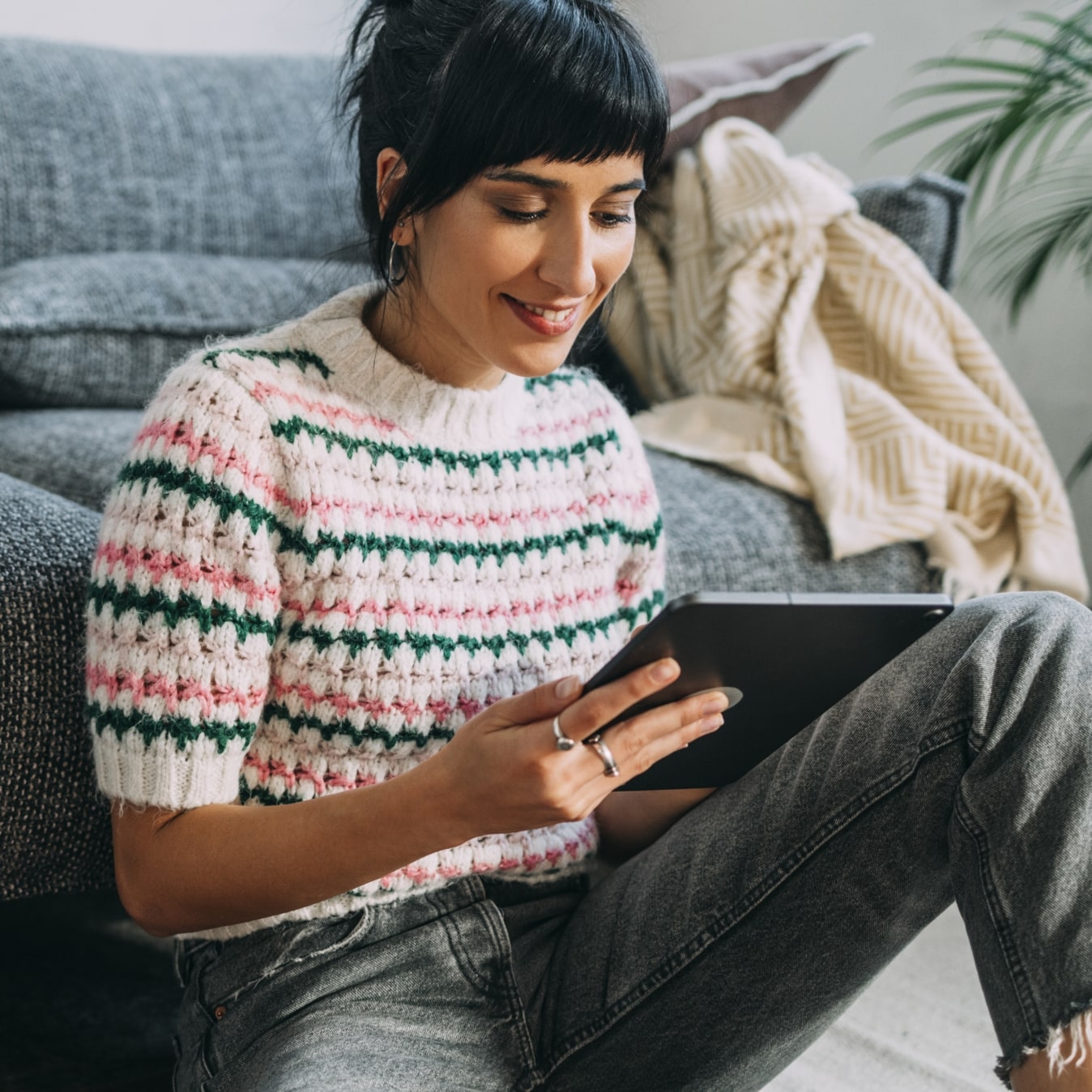 women in striped sweater looking at tablet in living room
