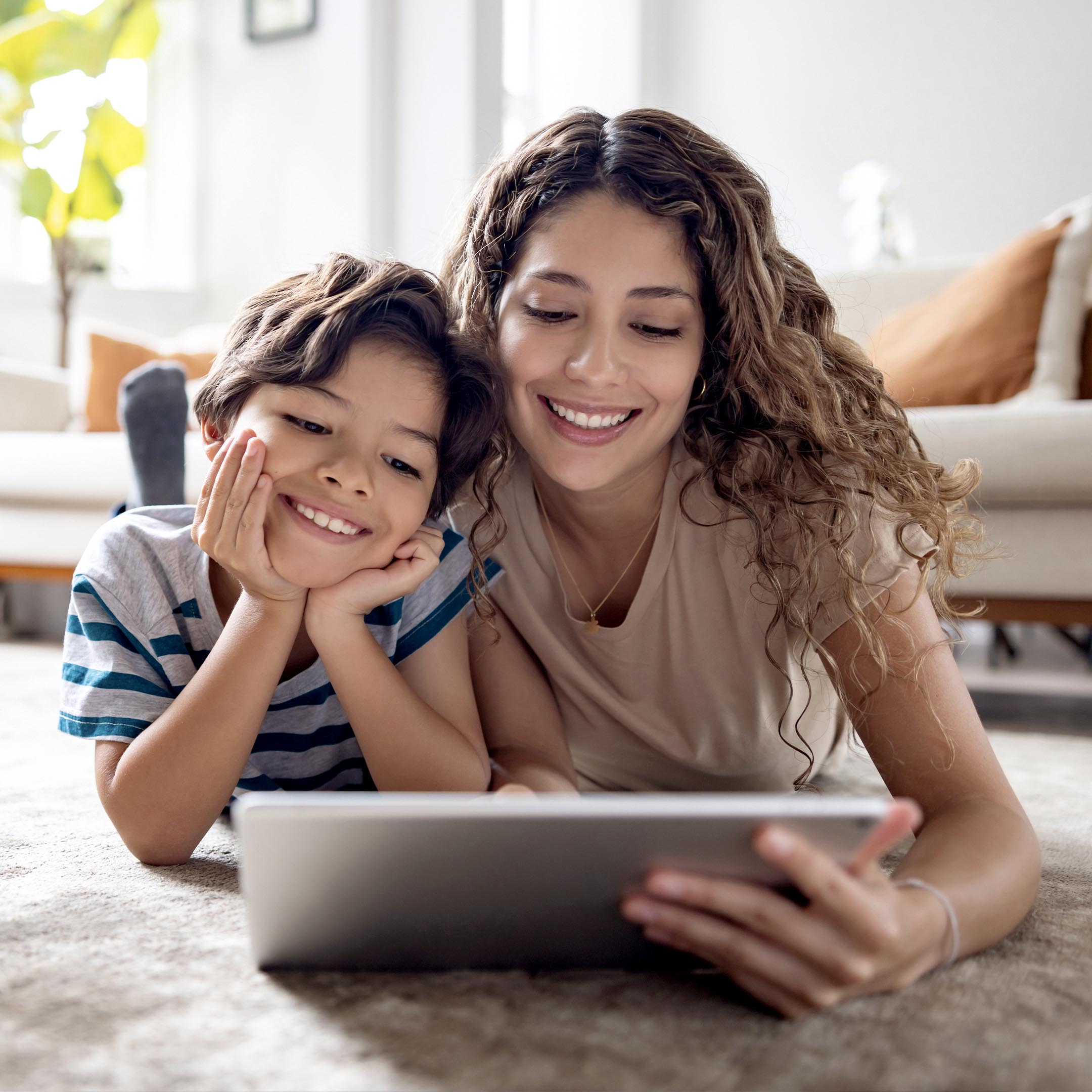 a women and a boy looking at a tablet in the living room smiling