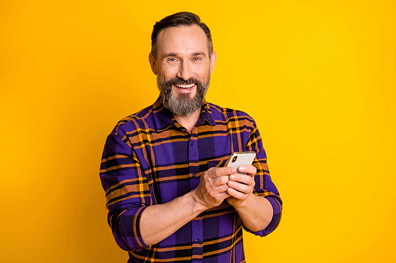 Smiling man holding a smartphone against a bright yellow background, representing easy signup for Blue Ridge Mobile internet service.