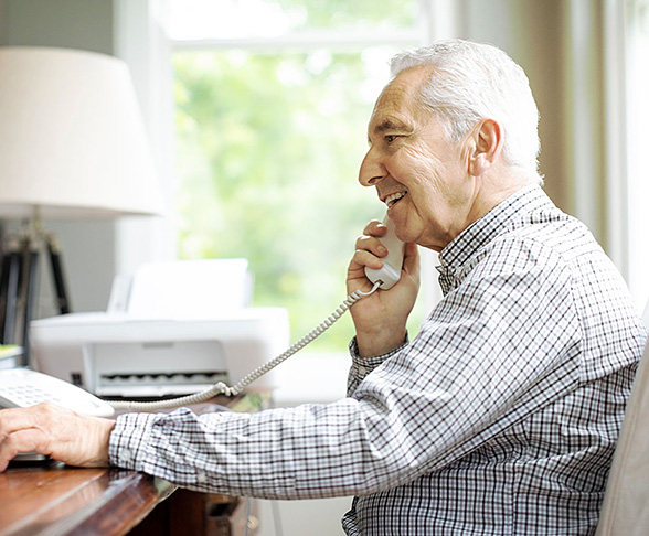 Person sitting at a desk and talking on a landline phone with a smile