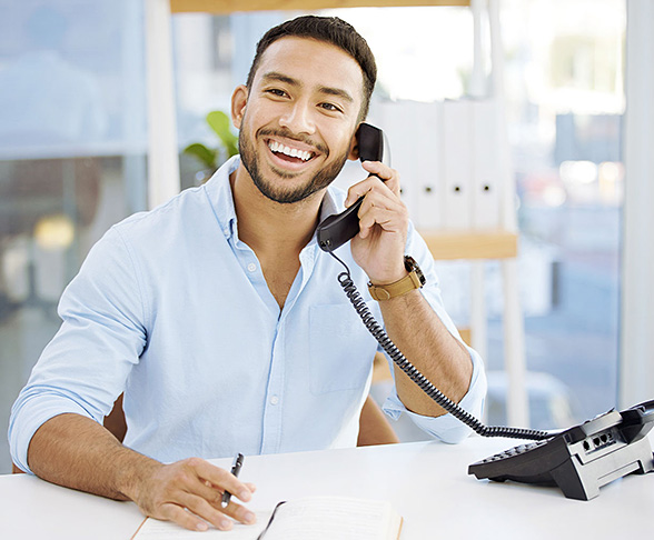Person smiling while answering a call on a desk phone in a bright office setting