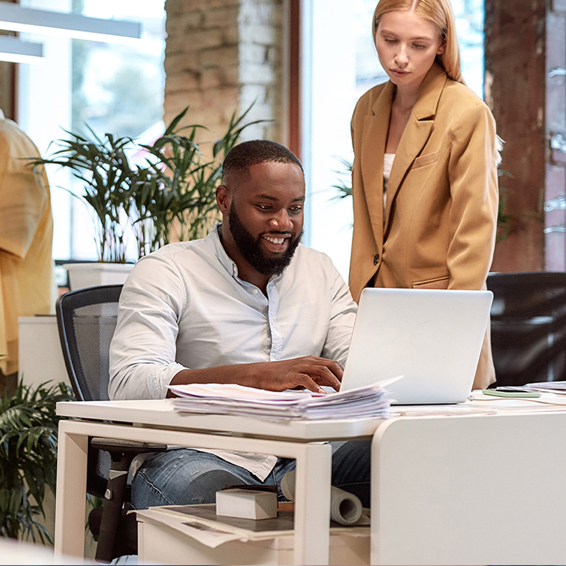Two coworkers reviewing something together on a laptop in a modern office